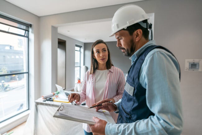 woman speaking to contractor in hard hat holding a clilpboard
